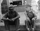 Negro and white man sitting on curb talking